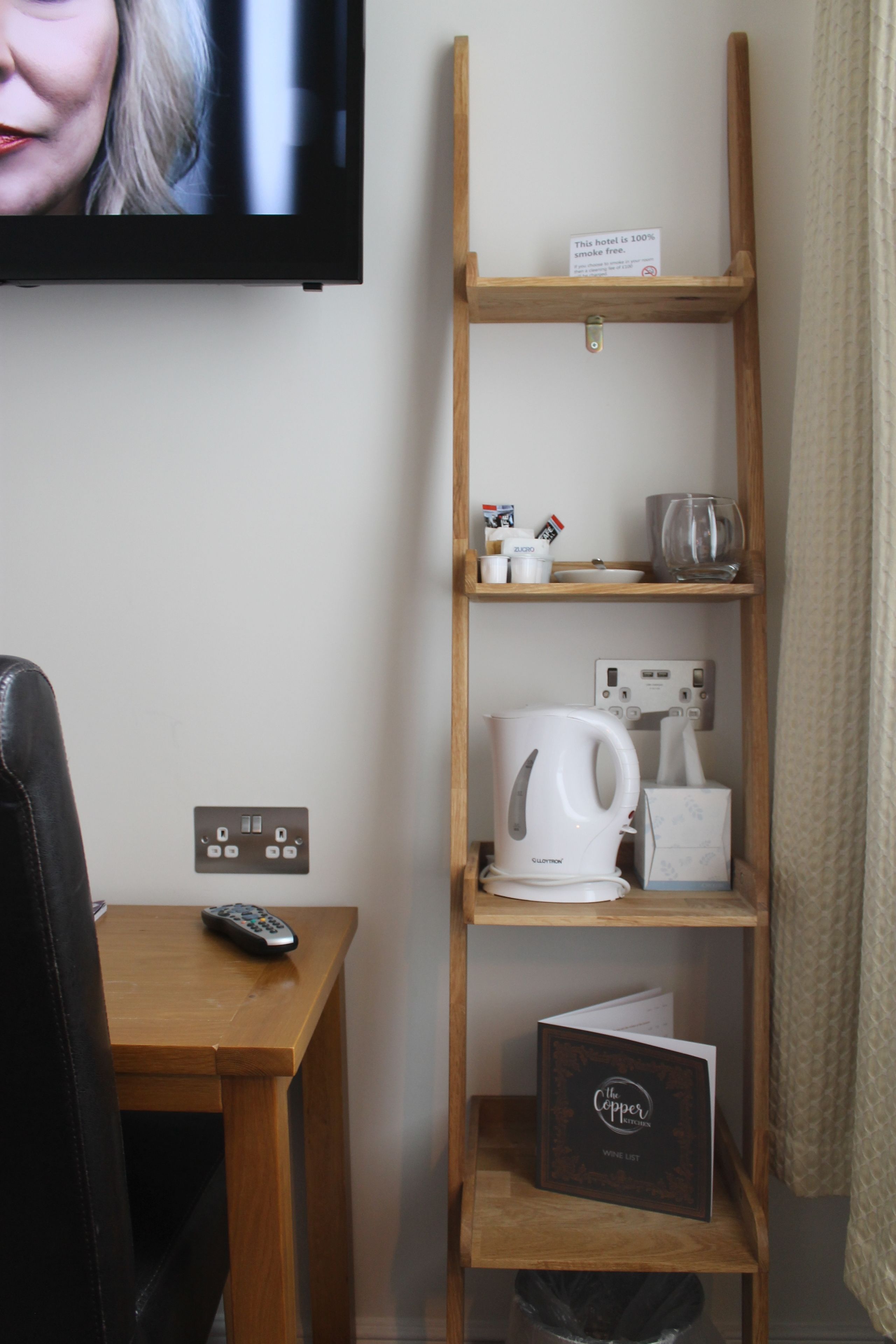 Habitación de hotel con estante de madera que sostiene una tetera, una taza y un letrero que indica que el hotel es 100% libre de humo.