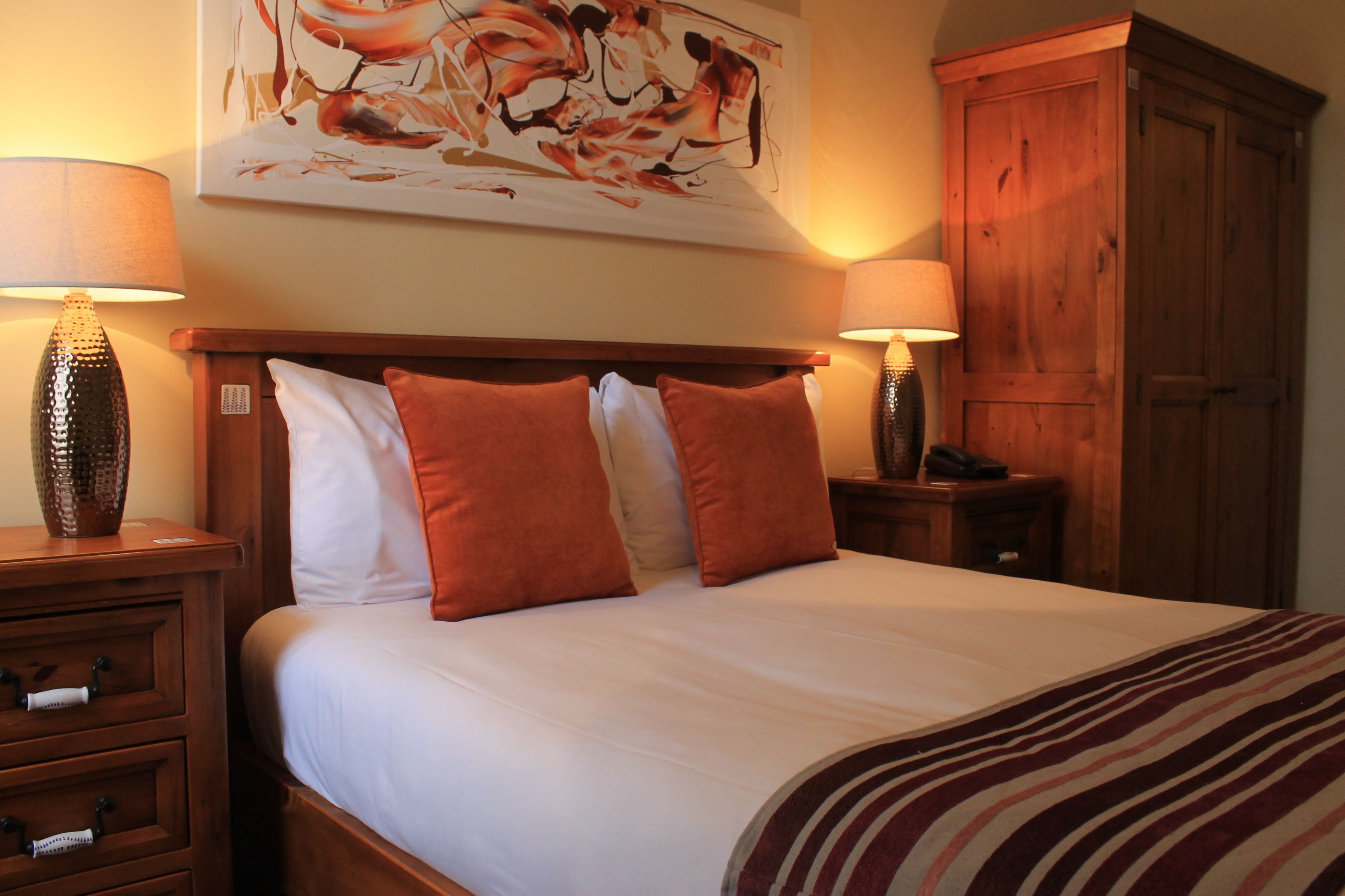 A neatly made bed with white and orange bedding, two bedside tables with lamps, and a wooden wardrobe.