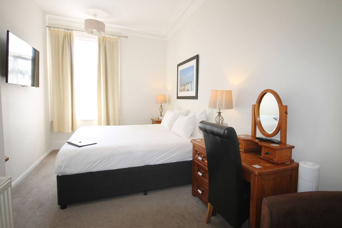 Een hotelkamer met een bed, nachtkastje, lamp, spiegel en een foto aan de muur.