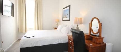 A hotel room with a bed, bedside table, lamp, mirror, and a picture on the wall.