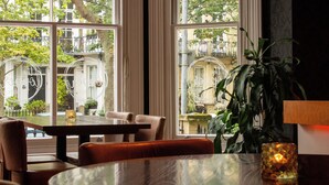 Un coin repas avec une table et des chaises, de grandes fenêtres donnant sur l’extérieur et une plante en pot.