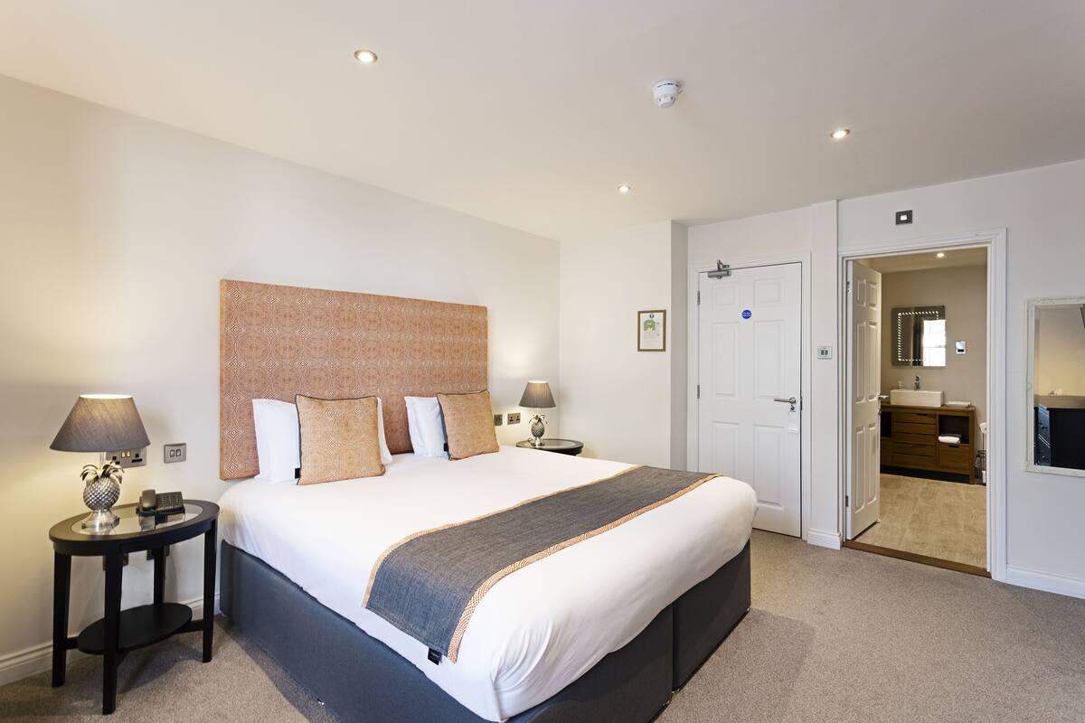 Een moderne hotelkamer met een groot bed, twee nachtkastjes met lampen, een hoofdeinde en een deur naar een badkamer.