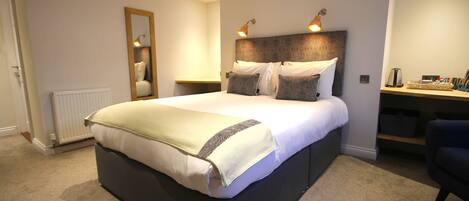 A neatly made bed with a headboard, bedside lamps, and a small table with a lamp and a basket.