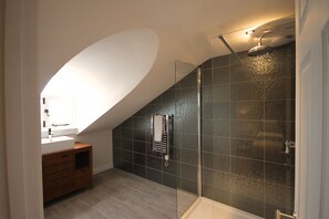 Un baño moderno con ducha de vidrio, tocador de madera y lavabo blanco.