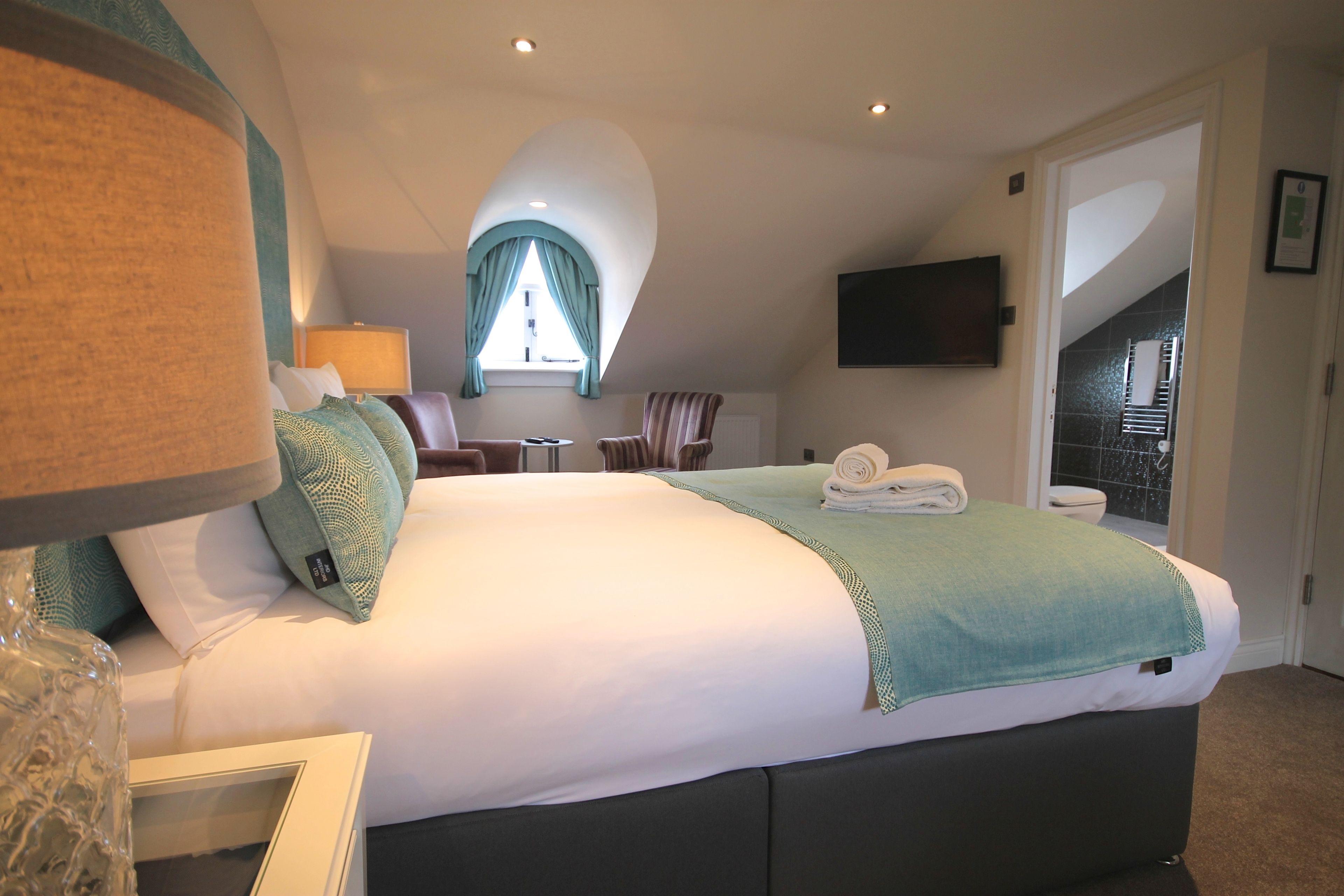A hotel room with a large bed, a TV mounted on the wall, a window with curtains, and a view of the outside balcony.
