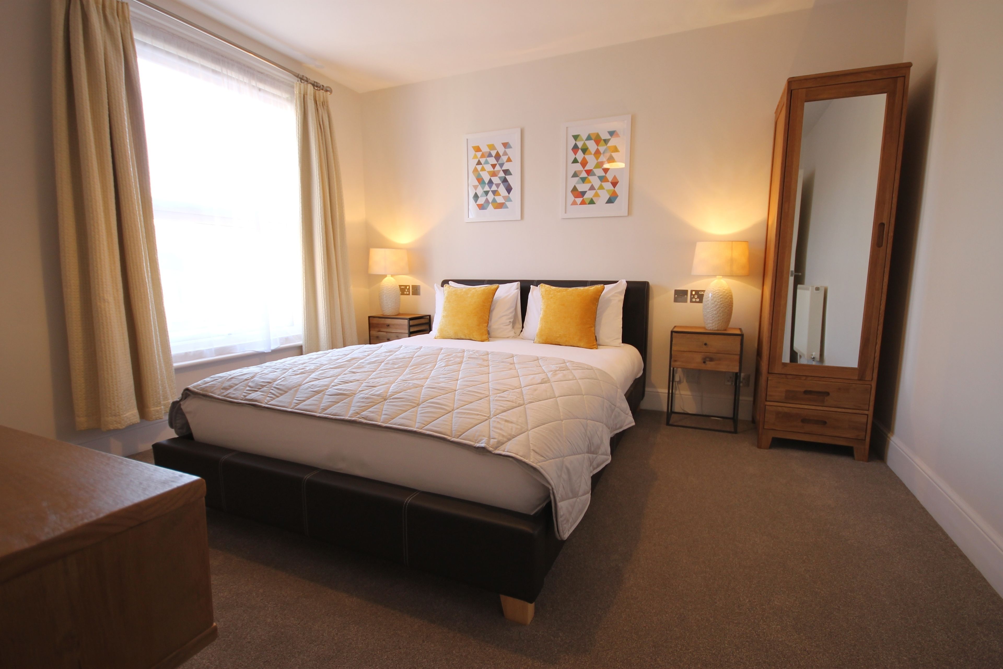 A bedroom with a bed, bedside tables, a mirror, and two wall art pieces.