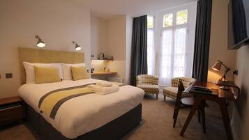 A hotel room with a large bed, a desk, a chair, and a television.