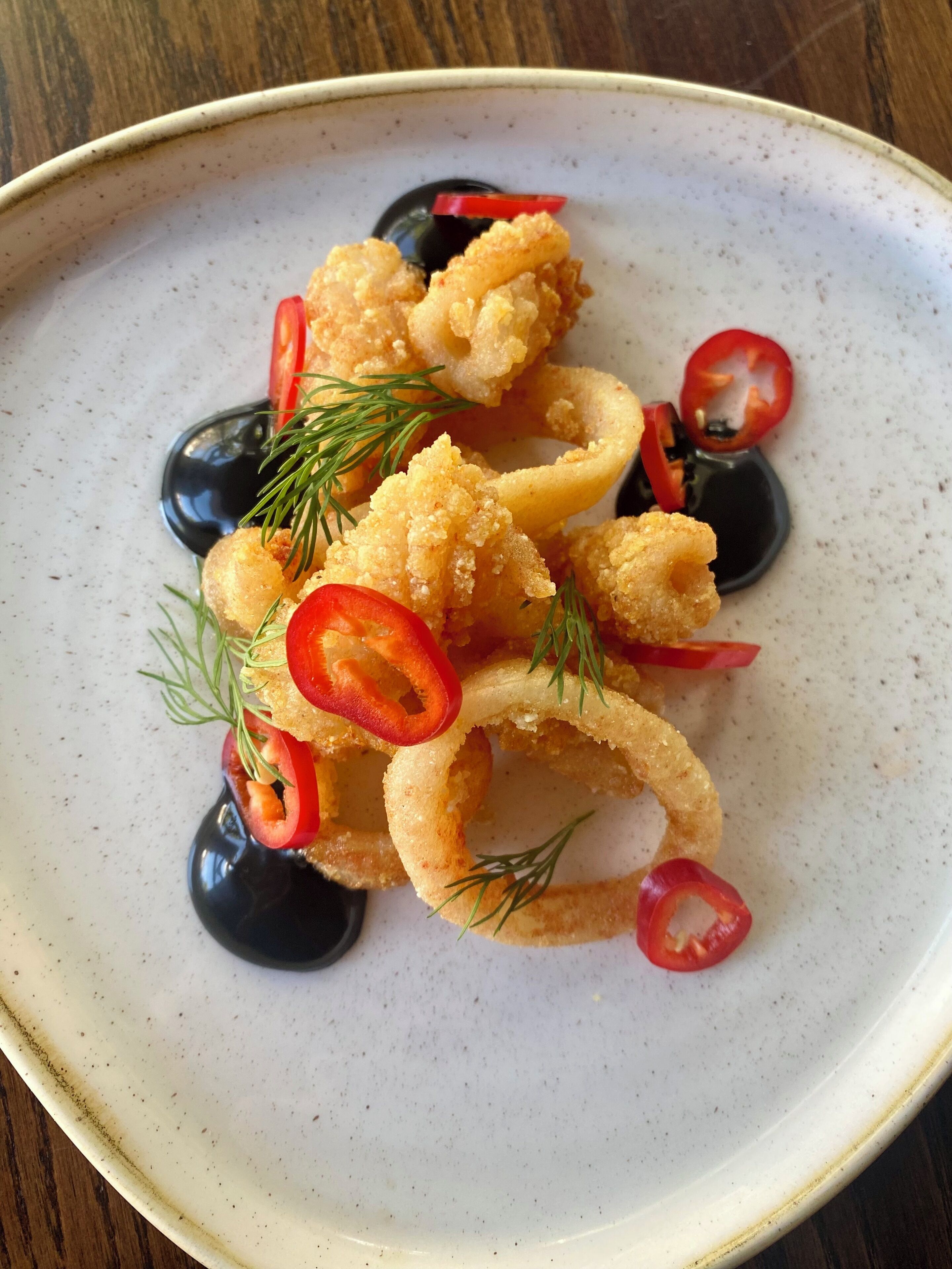 A plate of food with fried items, possibly calamari, garnished with red chili slices and dill.