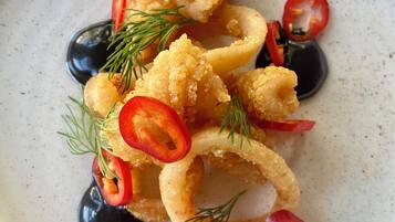 A plate of food with fried items, possibly calamari, garnished with red chili slices and dill.