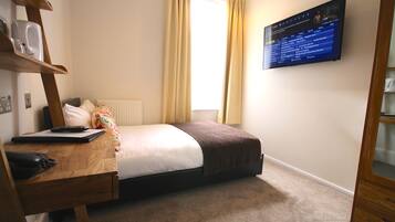 A bedroom with a bed, a desk with a computer, a telephone, and a TV mounted on the wall.