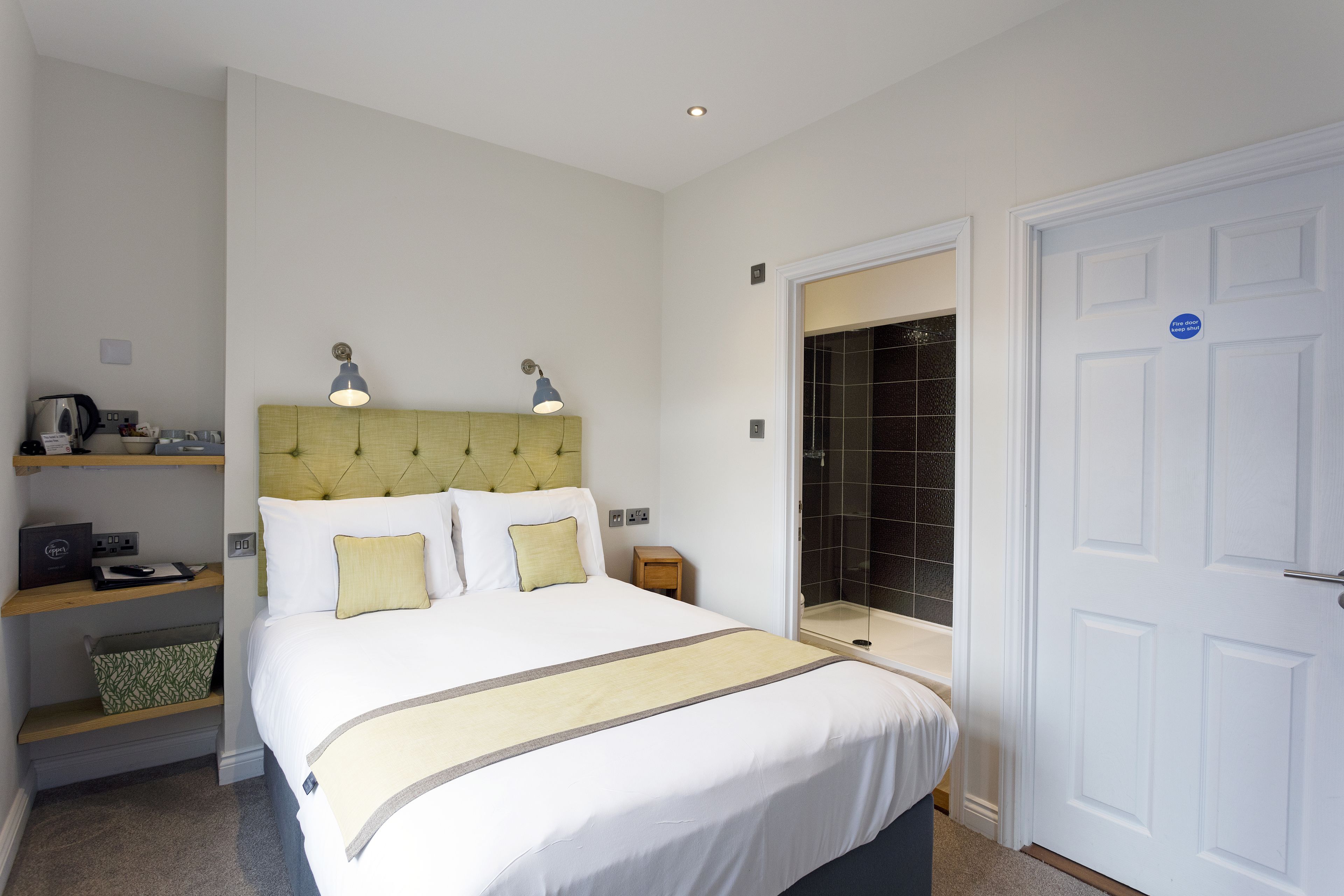 Habitación de hotel con cama, mesitas de noche, armario y baño con ducha e inodoro.