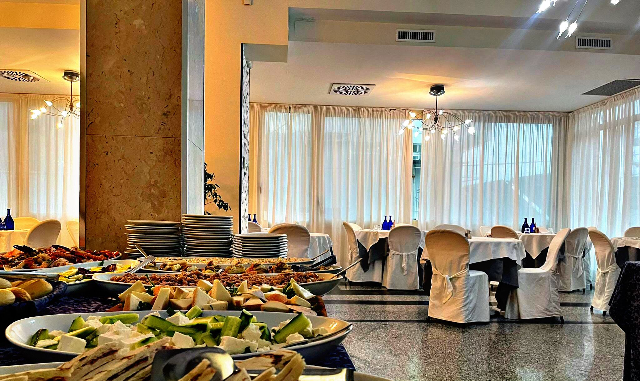 A banquet hall with round tables covered with white tablecloths, chairs with white covers, and a large pillar in the center.