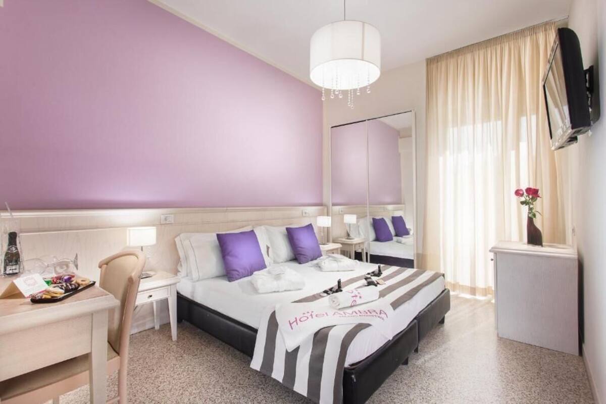 A hotel room with a bed, a desk, a chair, a TV, and a mirror.