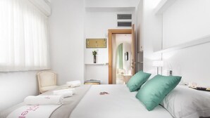 A hotel room with a neatly made bed, a chair, a bedside table with a lamp, and a view of the hallway. - Hotel Ambra (Cervia)