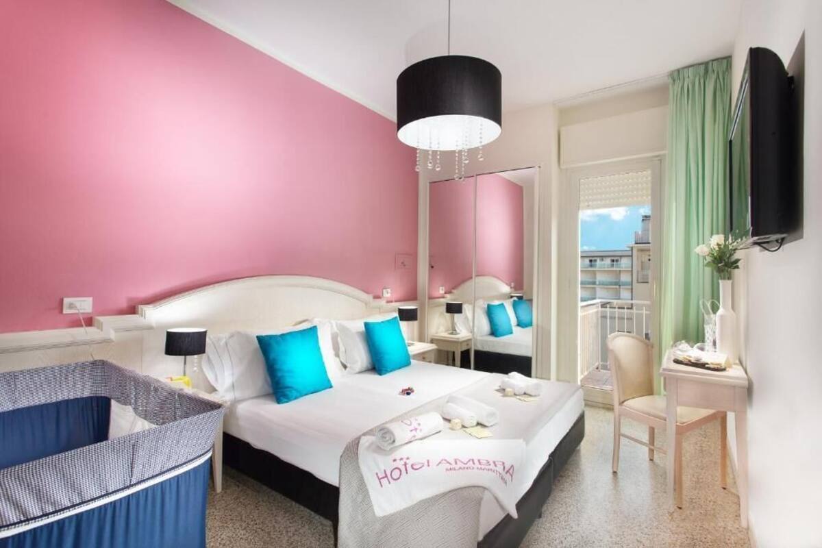 A hotel room with a bed, bedside tables, a chair, a desk, a TV, and a balcony with a view.