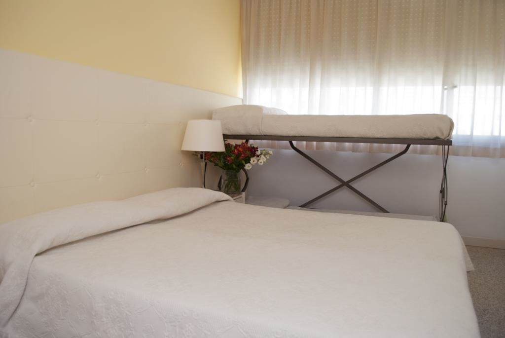 A hotel room with a bed, a small table with a lamp, and a window with curtains.