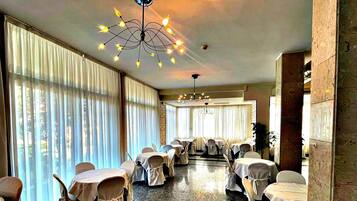 A hotel dining area with tables set for service, large windows with curtains, and a chandelier.