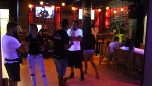 A bar with wooden walls and a TV screen displaying a movie. There are people sitting and standing around. - Asia Blue The Tavern Hacienda - Hostel (Ko Pha-ngan)