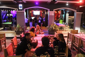 An indoor dining area with wooden tables and chairs, a pool table, and a bar area with stools. - Asia Blue The Tavern Hacienda - Hostel (Ko Pha-ngan)