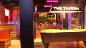 A billiards table in a room with a neon sign reading "THE TAVERN" and a bar area in the background. - Asia Blue The Tavern Hacienda - Hostel (Ko Pha-ngan)