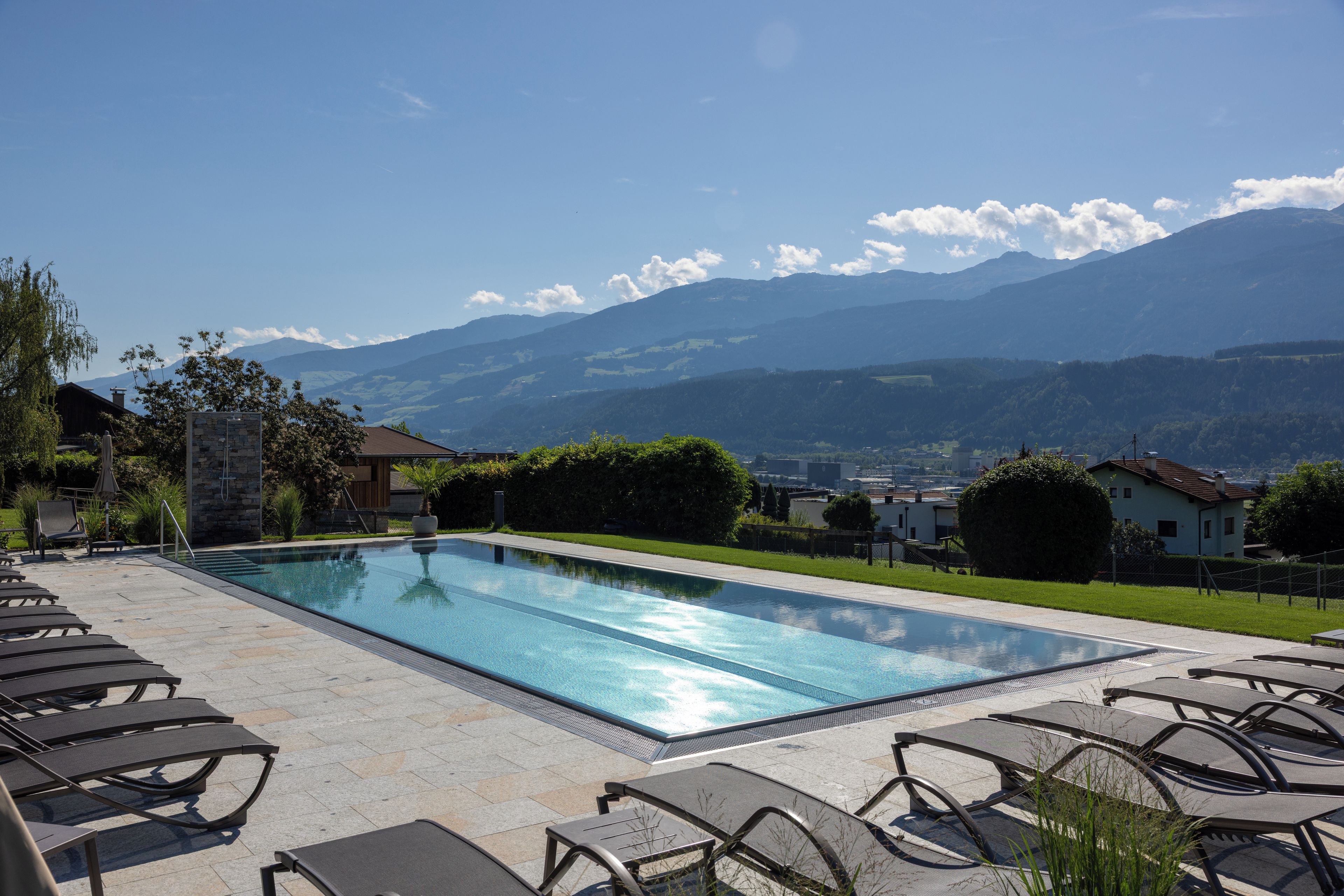 A swimming pool with lounge chairs, surrounded by a stone patio, with a mountain view in the background.