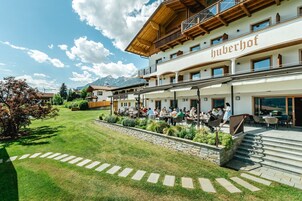 Un hotel con terrazza e area salotto all'aperto, immerso in un prato curato e un vialetto in pietra.