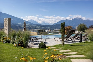 A pool area with lounge chairs, a stone pillar, and a view of mountains in the background. - Hotel Huberhof (Rum)
