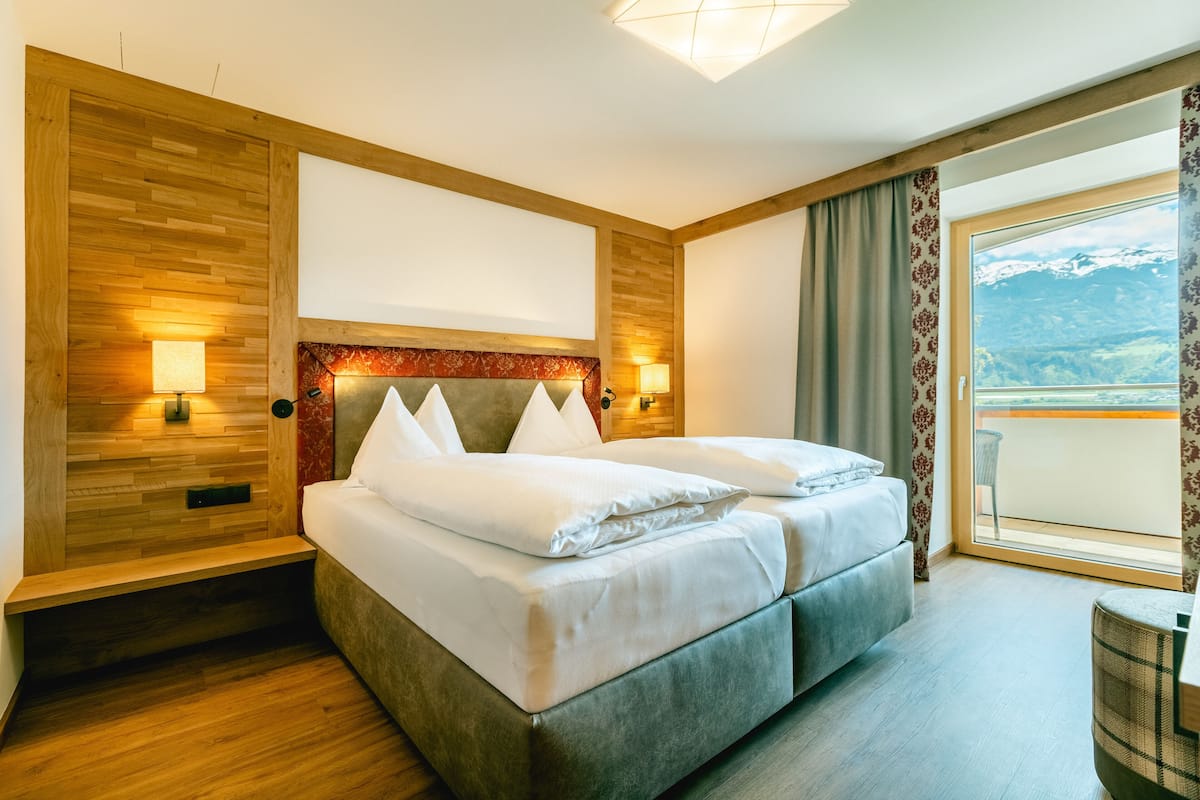 A double bed with a wooden headboard, two bedside lamps, and a view of mountains through a large window.