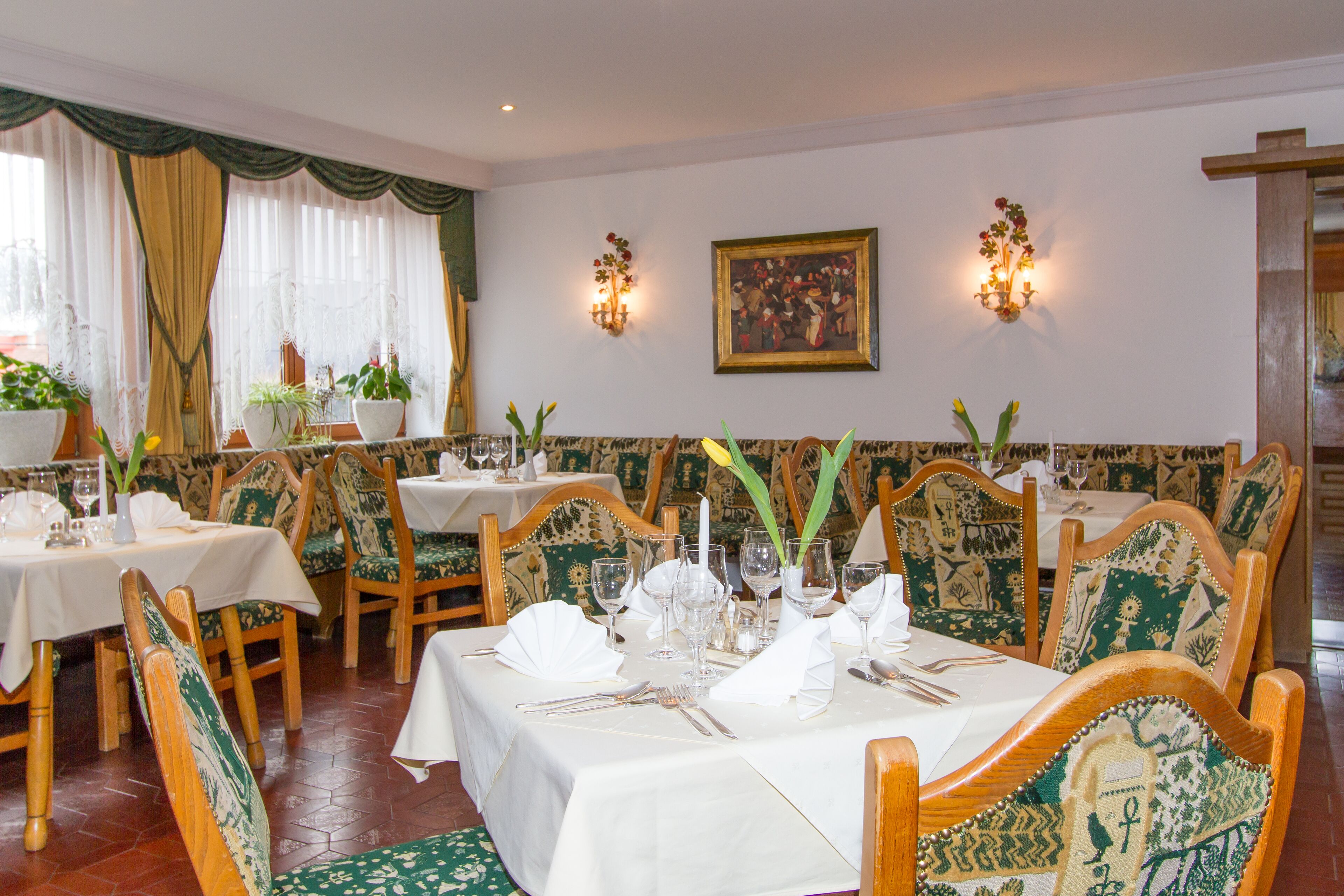 Un comedor con mesas dispuestas para el servicio, sillas de madera con tapicería estampada y lámparas fijadas a la pared.