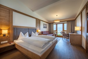A hotel room with a large bed, a desk, a chair, and a view of the outdoors.