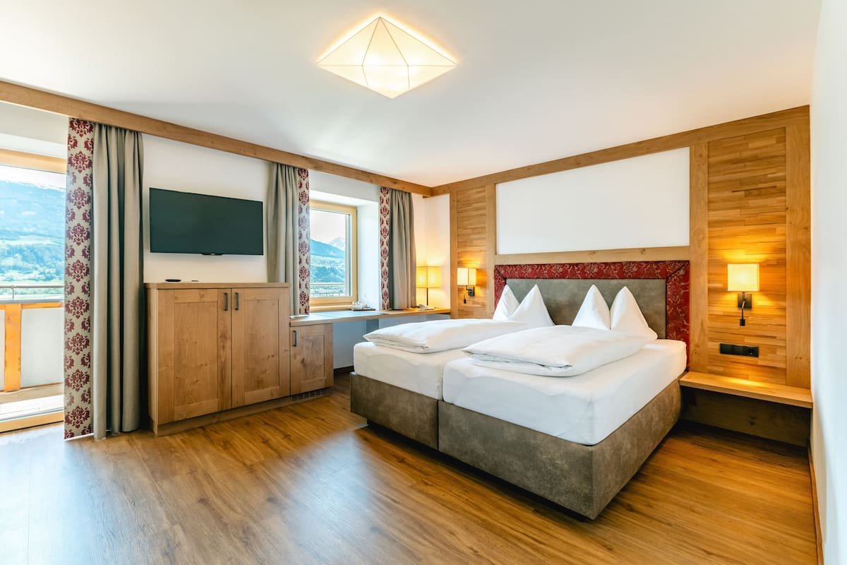 A modern hotel room with a large bed, wooden flooring, a TV, and a view of mountains.
