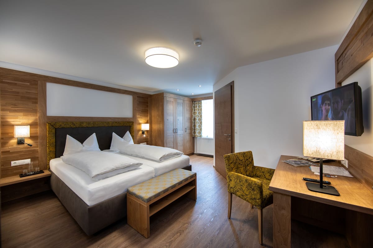 A modern hotel room with a large bed, a desk, a chair, and a television.