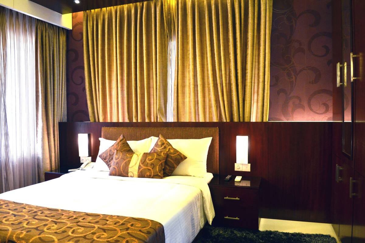 Une chambre d’hôtel avec un grand lit, deux tables de chevet, une commode, une armoire et des rideaux.
