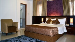 A hotel room with a large bed, a chair, a nightstand, and an air conditioning unit. - Hotel La Villa Western (Dhaka)