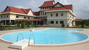 A swimming pool surrounded by a building with a red roof and a beige facade.