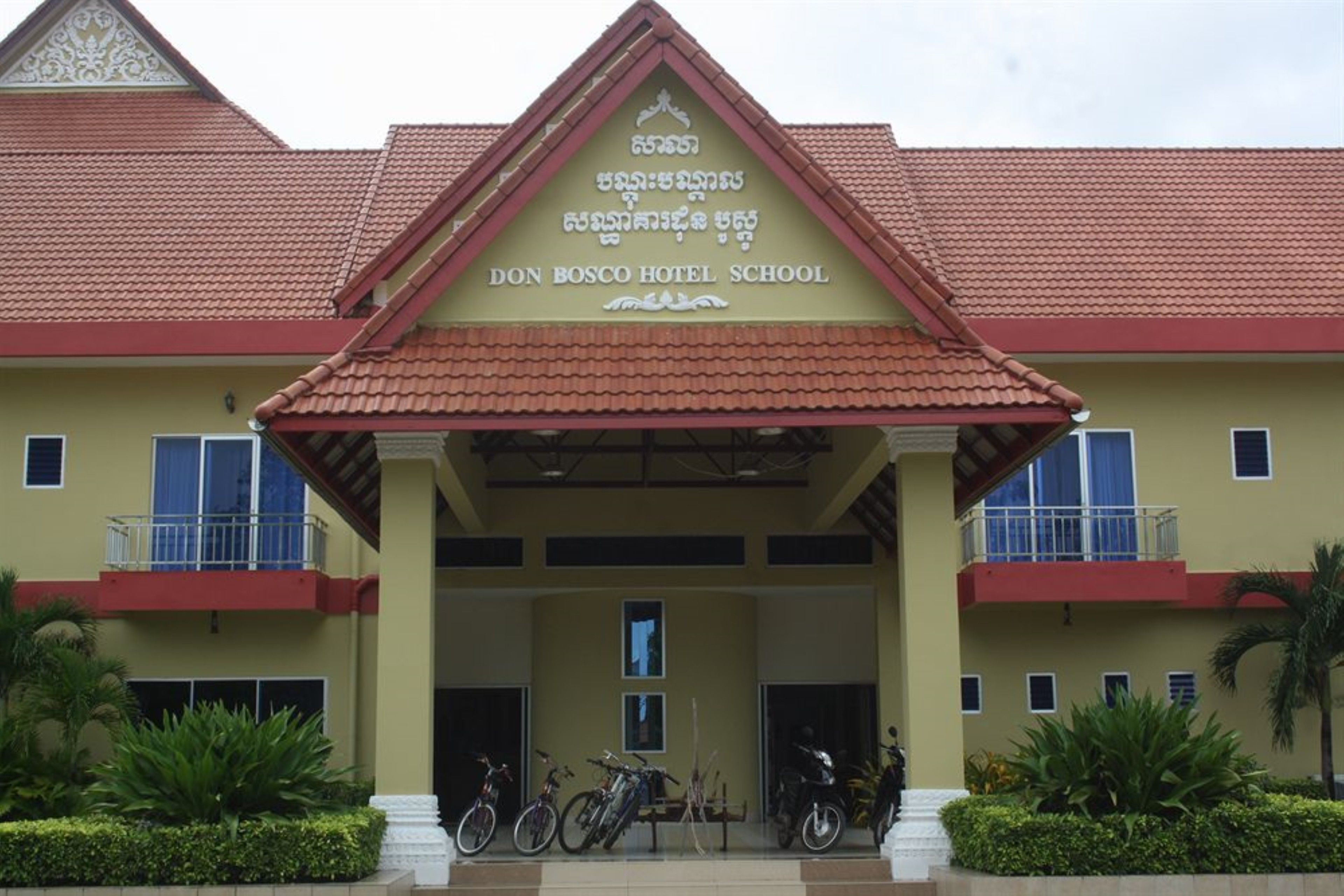 The exterior of Don Bosco Hotel School with a red-tiled roof, a central entrance, and a sign above.