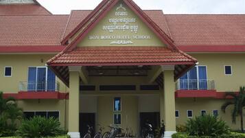The exterior of Don Bosco Hotel School with a red-tiled roof, a central entrance, and a sign above.