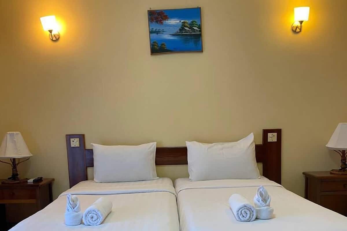 Een hotelkamer met twee enkele bedden, witte lakens en handdoeken. Er zijn wandlampen en een schilderij boven de bedden.