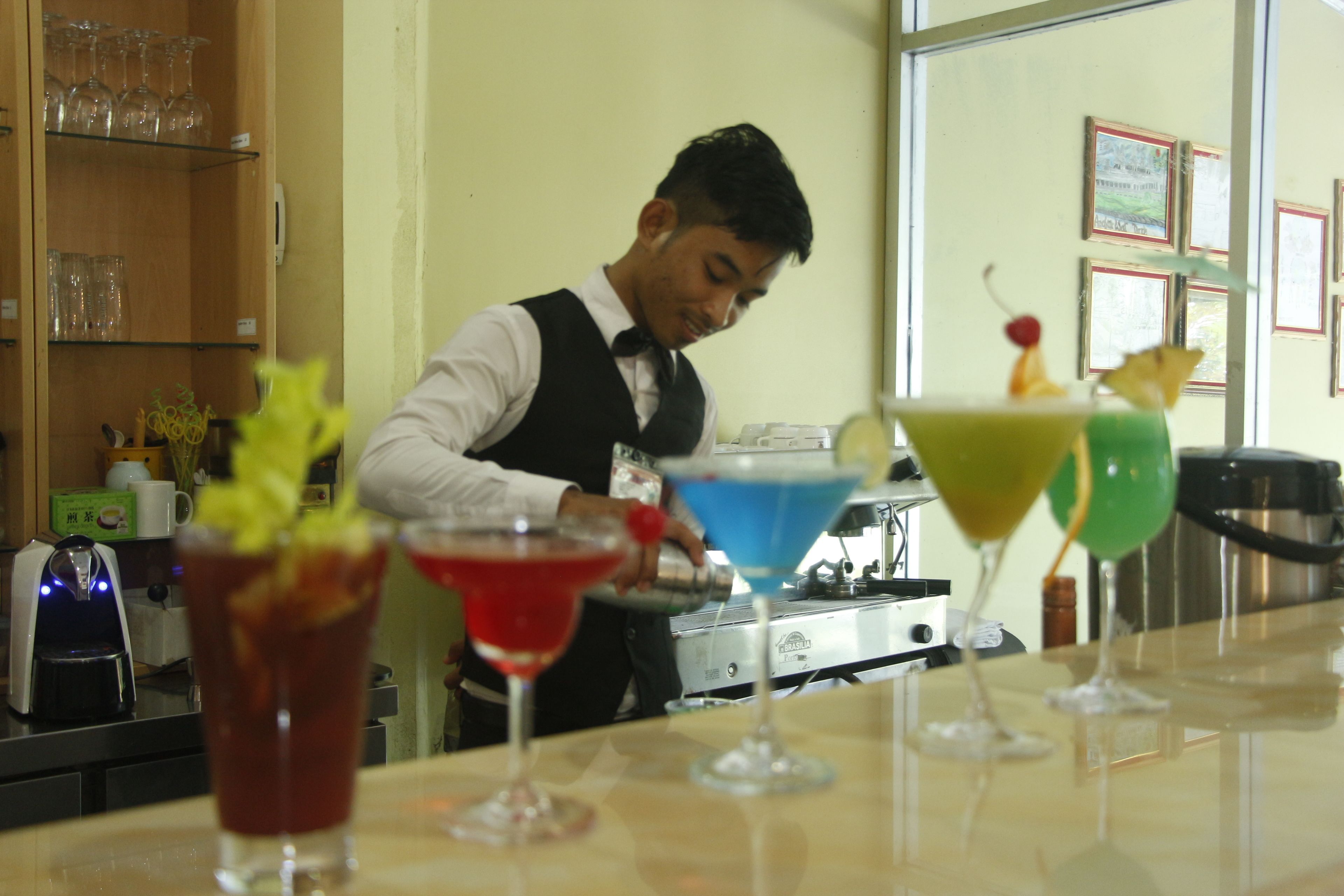 Zona de bar con un cantinero preparando bebidas. Varias cocteles coloridas se encuentran en la barra.