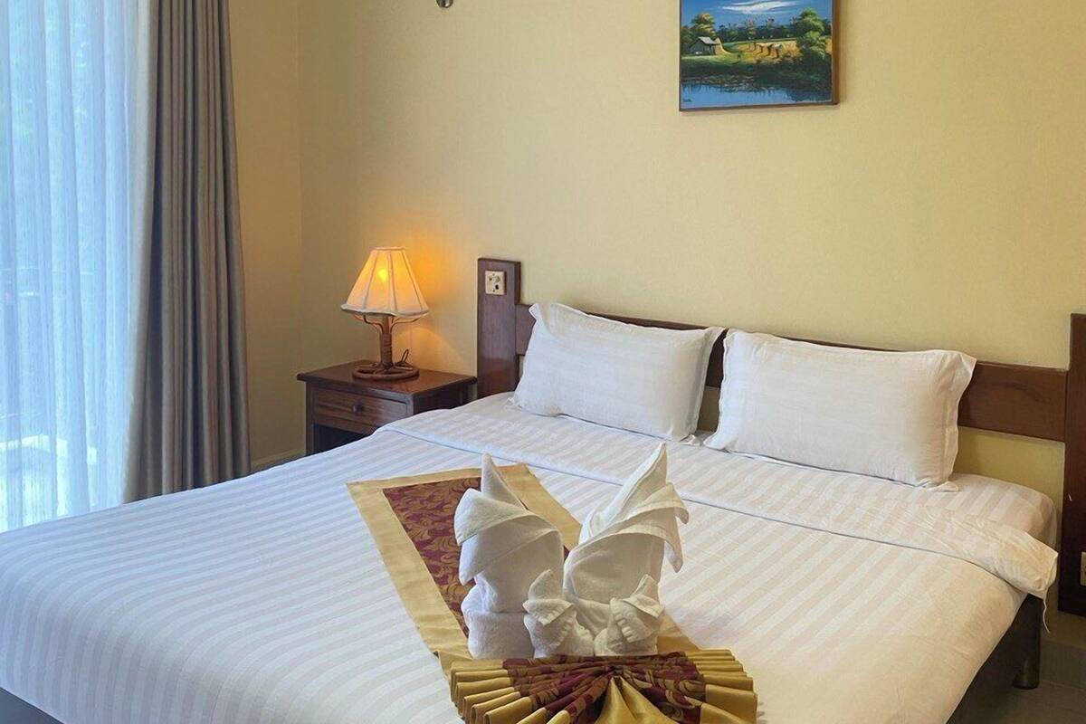 Een hotelkamer met een groot bed, een schilderij aan de muur, een lamp en een raam met gordijnen.