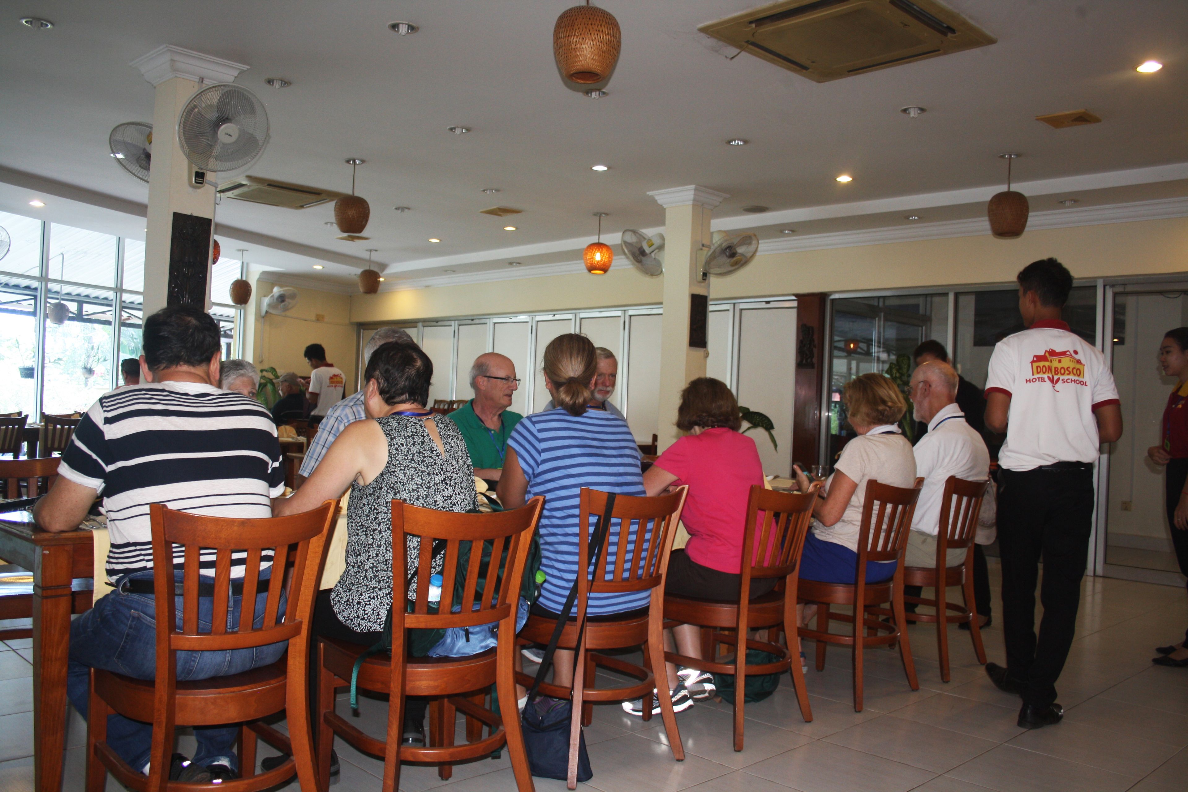 A restaurant with wooden chairs and tables, fans on the ceiling, and large windows.