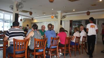 A restaurant with wooden chairs and tables, fans on the ceiling, and large windows.