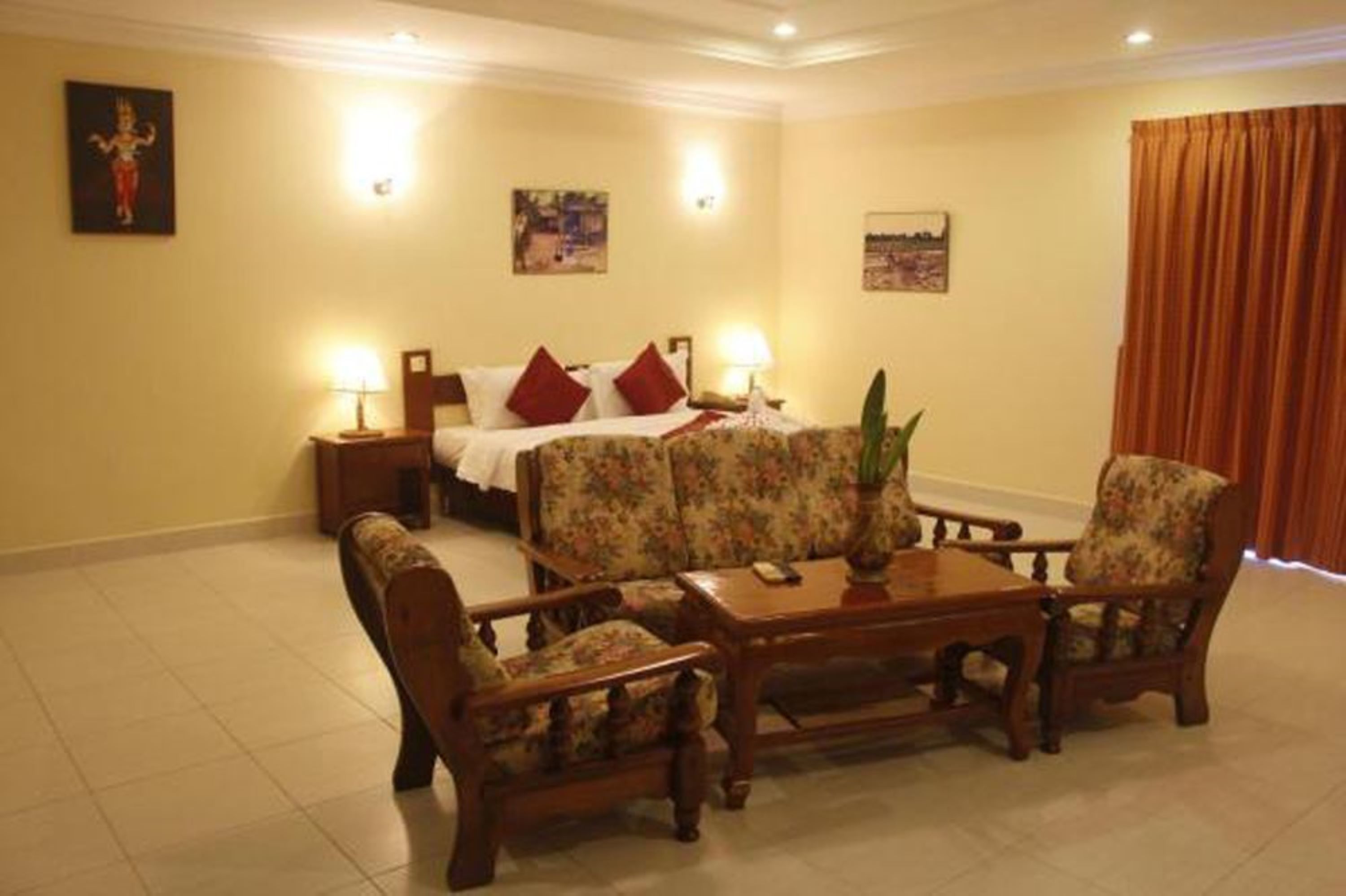 Une chambre d’hôtel comprenant un lit, deux tables de chevet, un canapé, deux fauteuils, une table basse et une plante en pot.