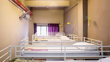 Um dormitório com beliches, uma janela com cortinas roxas e uma luminária presa à parede.