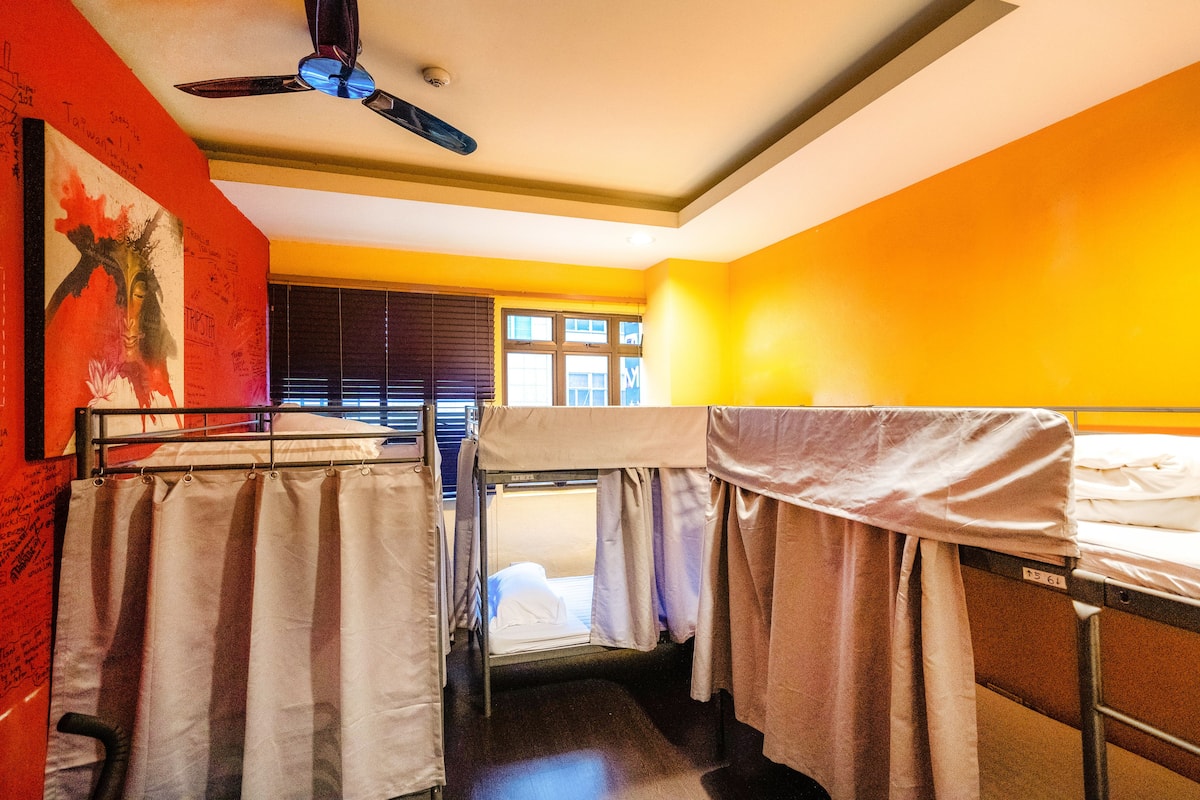 Ein Schlafsaalzimmer mit Etagenbetten, einem Deckenventilator und einem Fenster mit Jalousien.