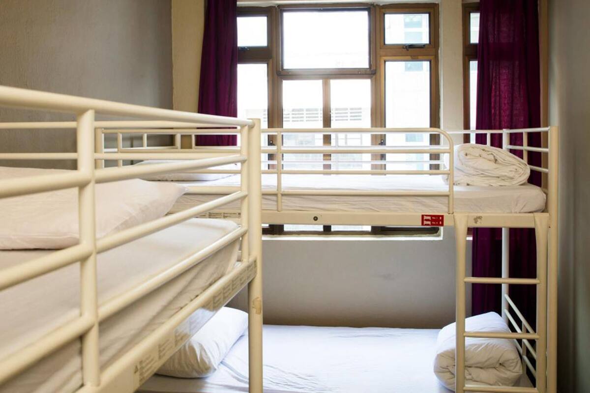 Ein Schlafsaalzimmer mit Etagenbetten, einem Fenster mit Vorhängen und Blick auf Gebäude.
