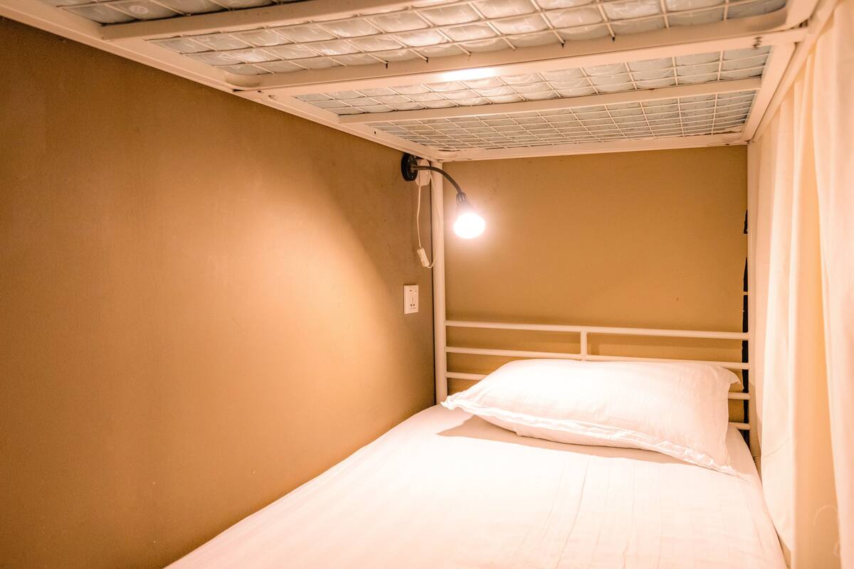 Ein Einzelbett mit weißer Bettwäsche in einem Zimmer mit beige gestrichenen Wänden und einer weißen Decke.