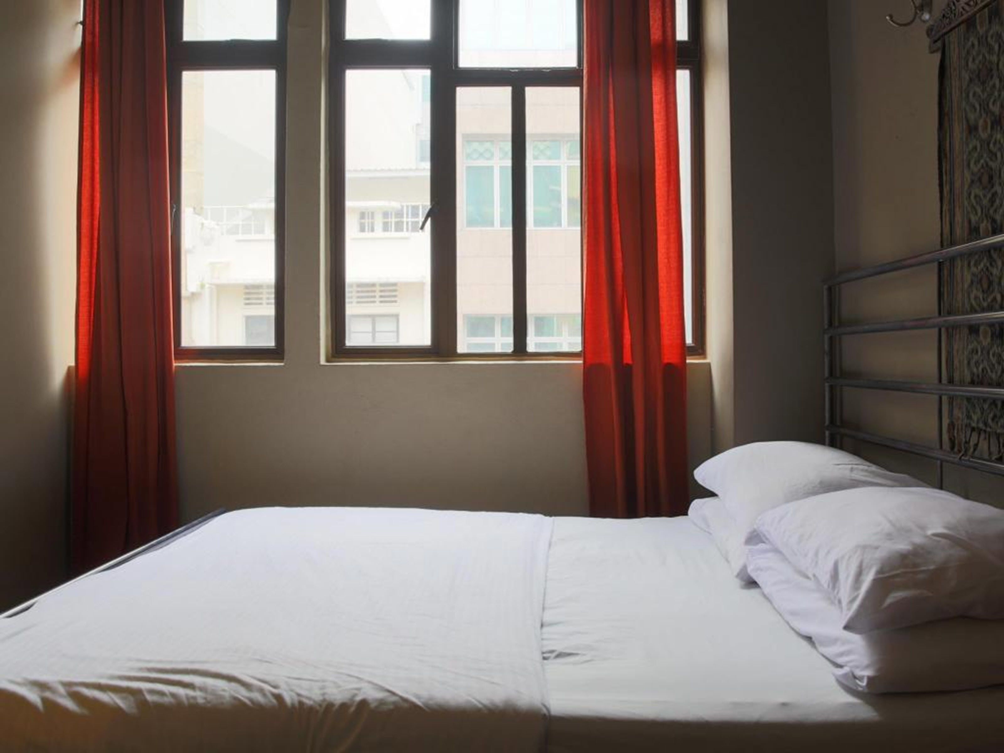 A bedroom with a bed, two windows with red curtains, and a metal headboard.