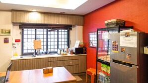 Une cuisine compacte équipée d’un four à micro-ondes, d’un réfrigérateur et d’une fenêtre avec des stores.