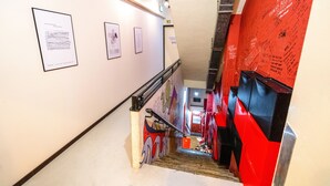 Un escalier muni d’une rampe, un mur rouge couvert de graffitis et des documents encadrés accrochés au mur.